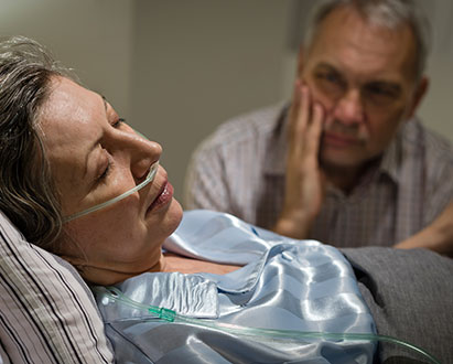 Sick elderly woman in hospital with husband looking on